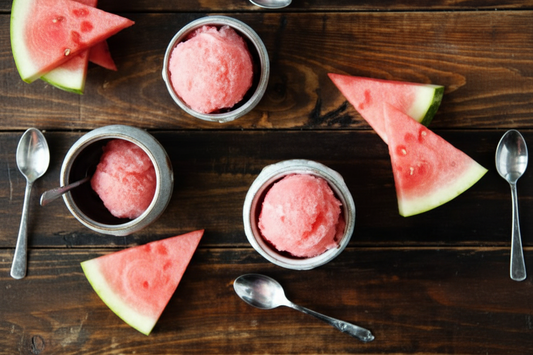 Pink ice cream in metal bowls with watermelon slices on a wooden surface