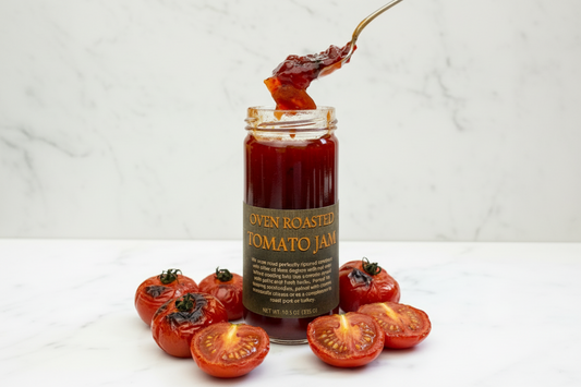 Jar of oven roasted tomato jam with a spoonful being lifted out, on a white marble surface.