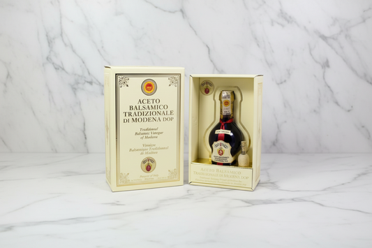 A traditional balsamic vinegar bottle with a white label, packaged in a box with the text 'ACETO BALSAMICO DI MODERNA DOP' and a golden emblem.