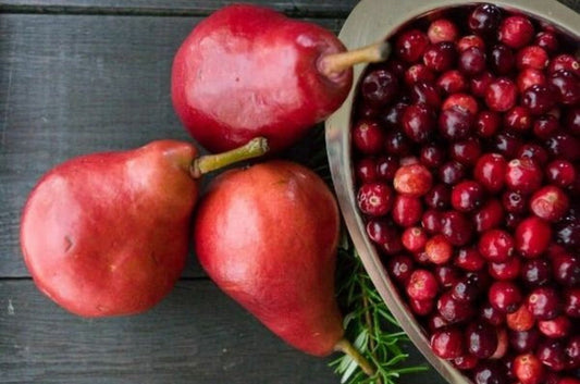 A bowl of cranberries at the top and three whole pears at the bottom with a rosemary sprig on a dark wooden surface.
