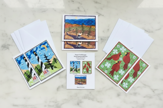 A set of six notecards with envelopes, featuring art prints of North Carolina-related symbols and landscapes, laid out on a wooden surface.
