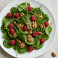 Spinach salad with raspberries and walnuts on a white plate
